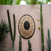 Een mooie grote ronde schaal in een natuurlijke kleur, gemaakt van bananenbladeren en met een zwarte grafische print . een eyecatcher als muurdecoratie 